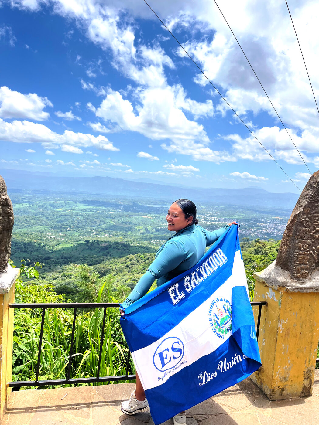 Patricia Torres holding the El Salvador flag above a green valley